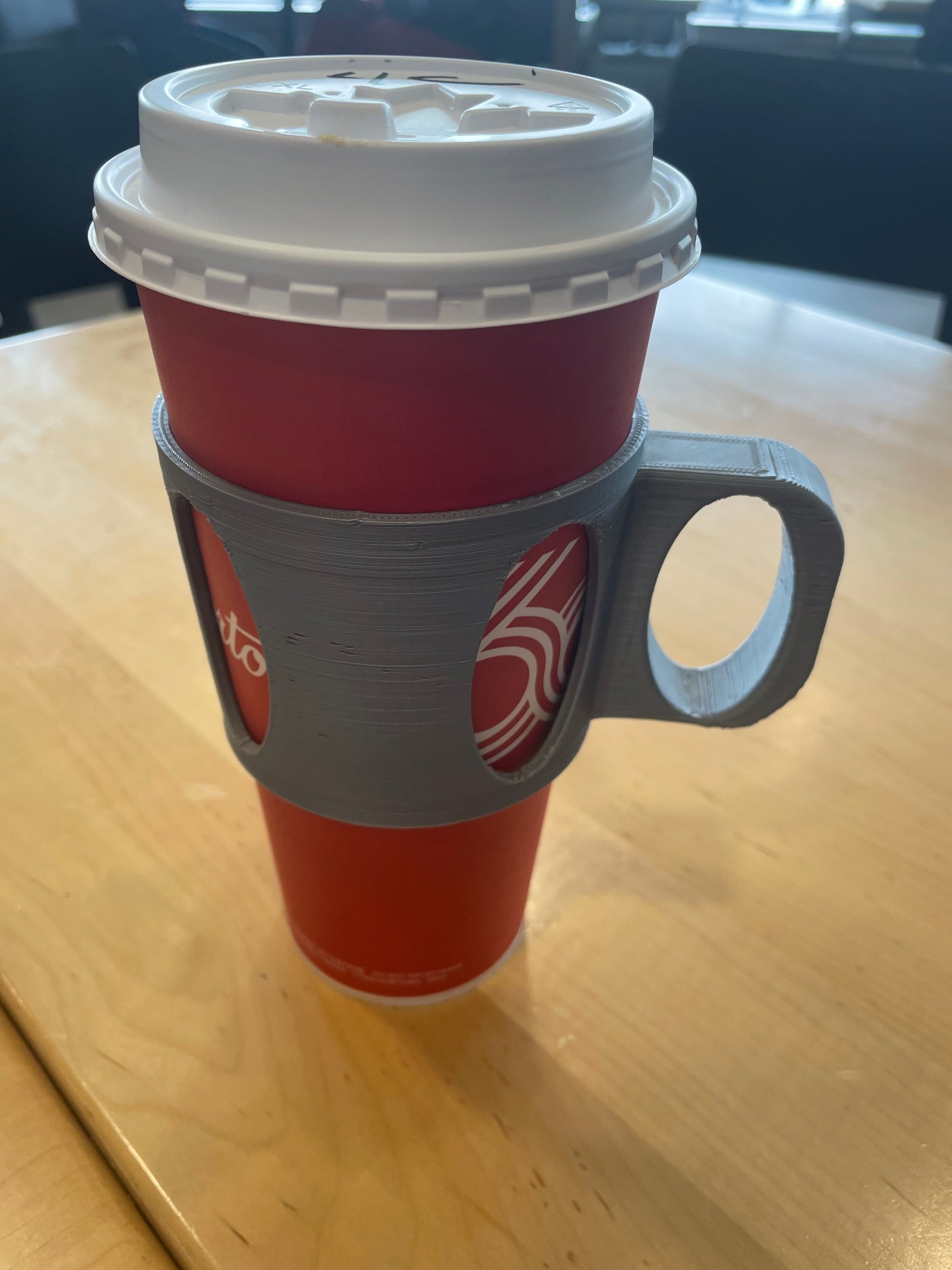 Red paper coffee cup with a grey 3D printed cup holder sleeve with handle.