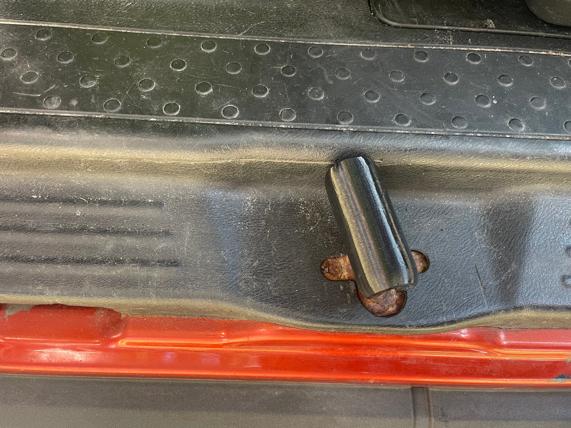 Close-up of a black car door latch with visible rust on the screw.
