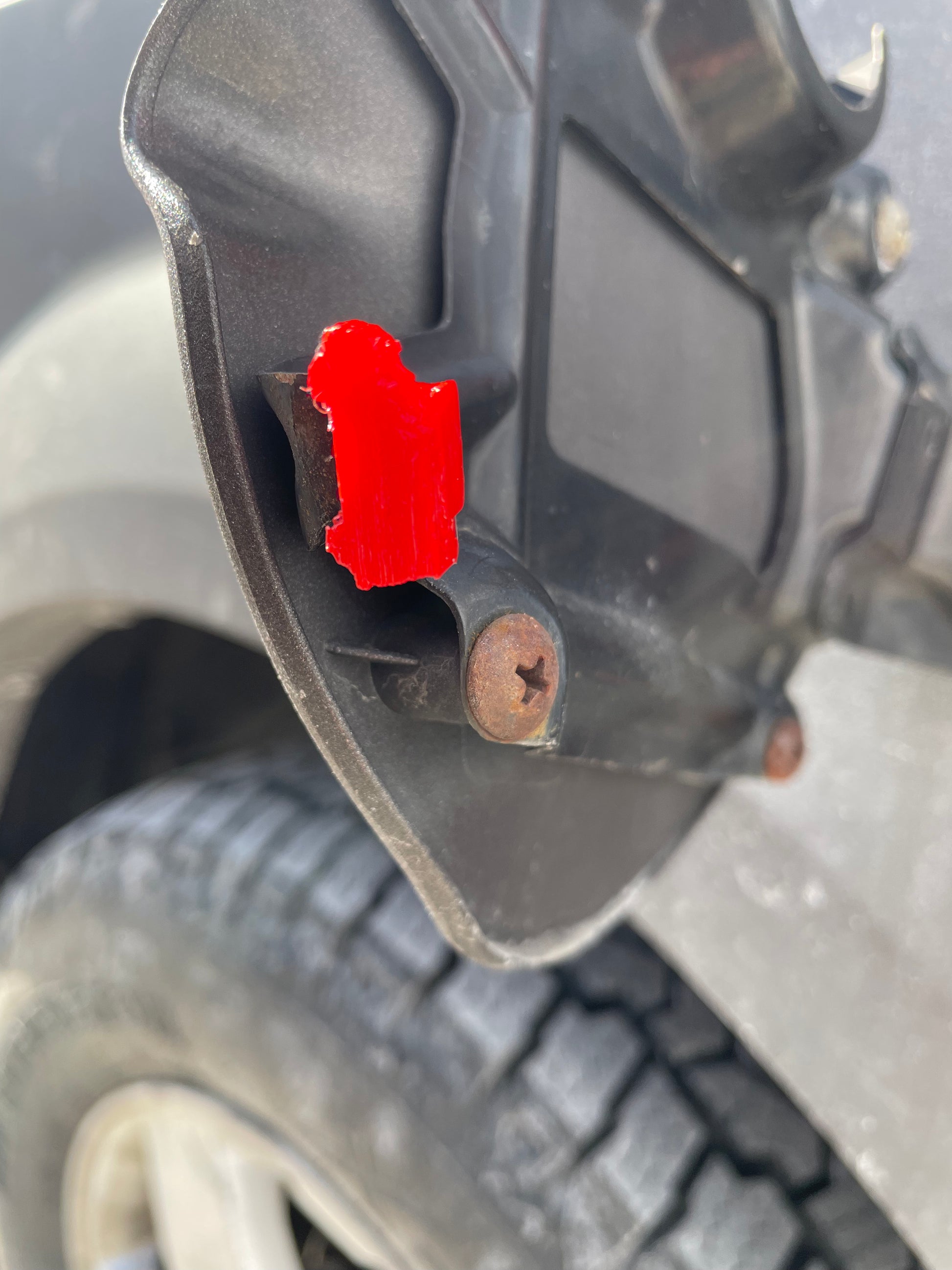 Close-up of a car's gas tank door with red tape and rusty screws.