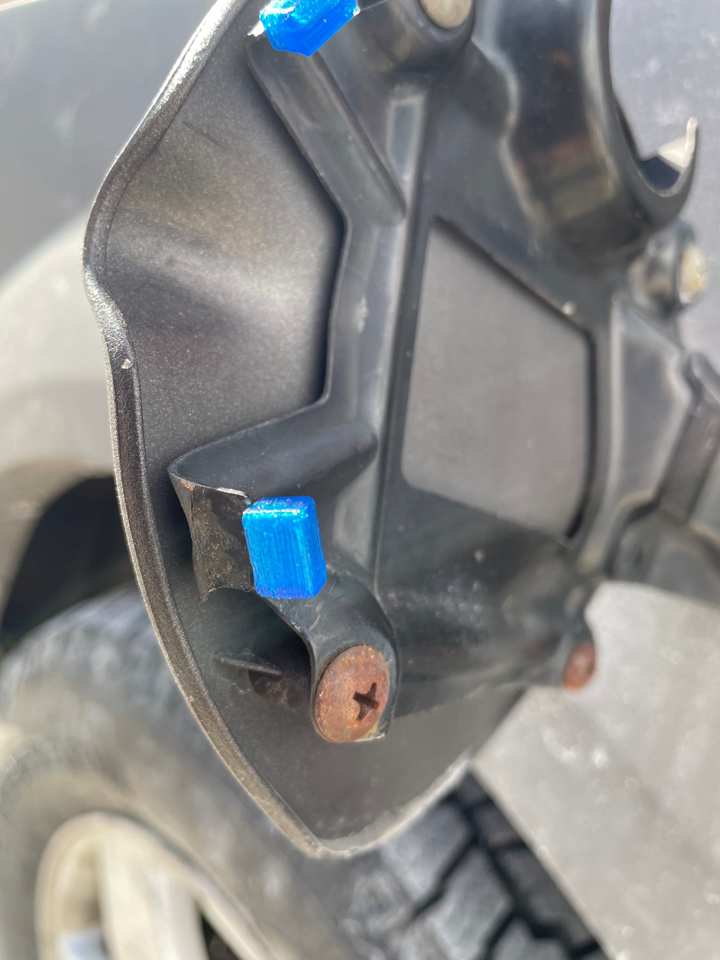 Close up of blue 3D printed gas door hinge repair clips on a black car gas door.
