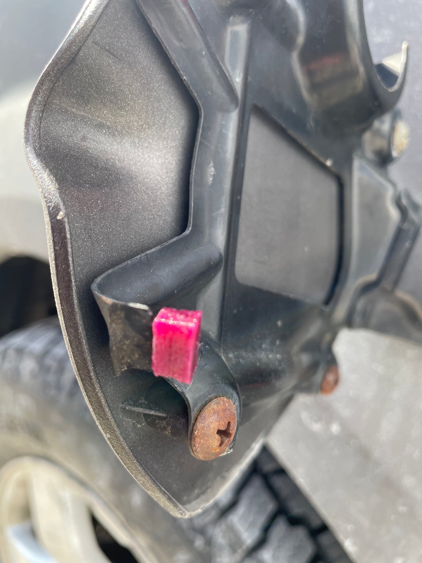 Close up of a black plastic car part with a pink cube and rusty screw.