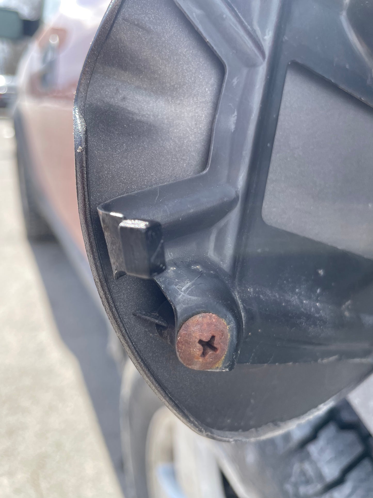 Close-up of a car's dark gray fuel door hinge with a rusty screw.