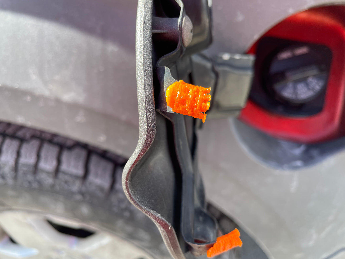 Close-up of car fuel door and cap tether with orange safety retainers.