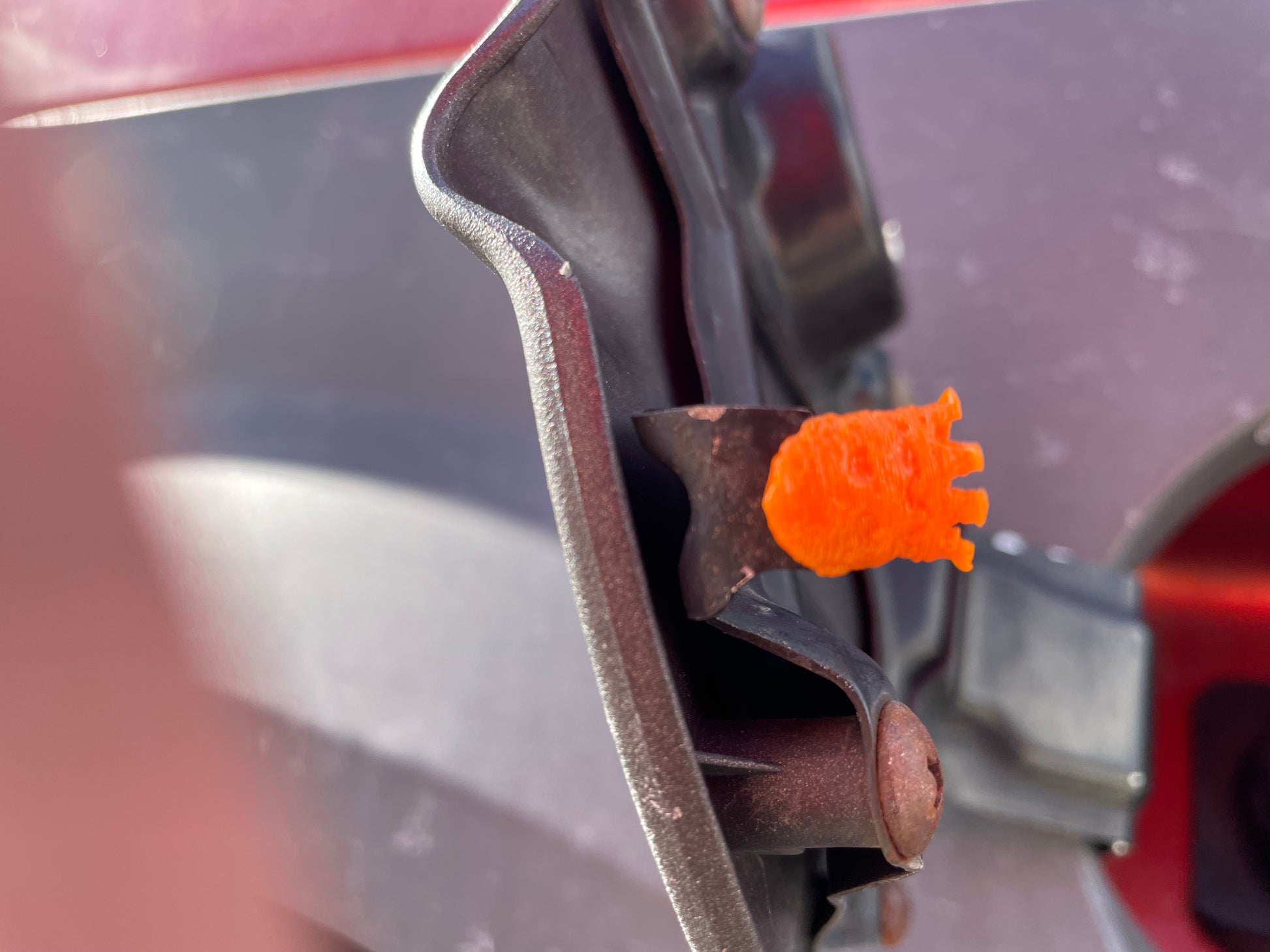 Fuel door hinge with an orange retaining clip installed.