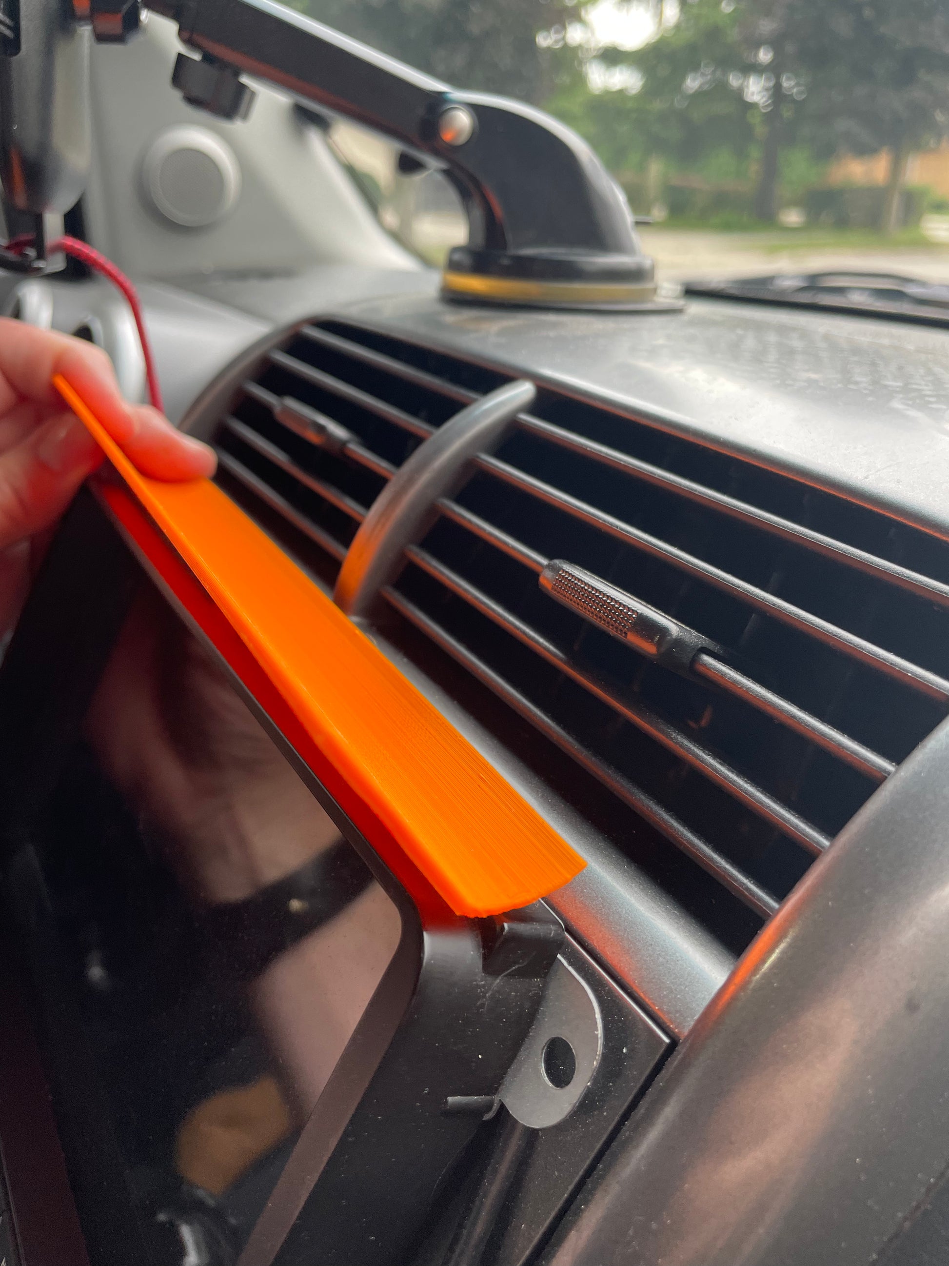Orange plastic tool removing car radio from dashboard air vent. Car audio installation concept.