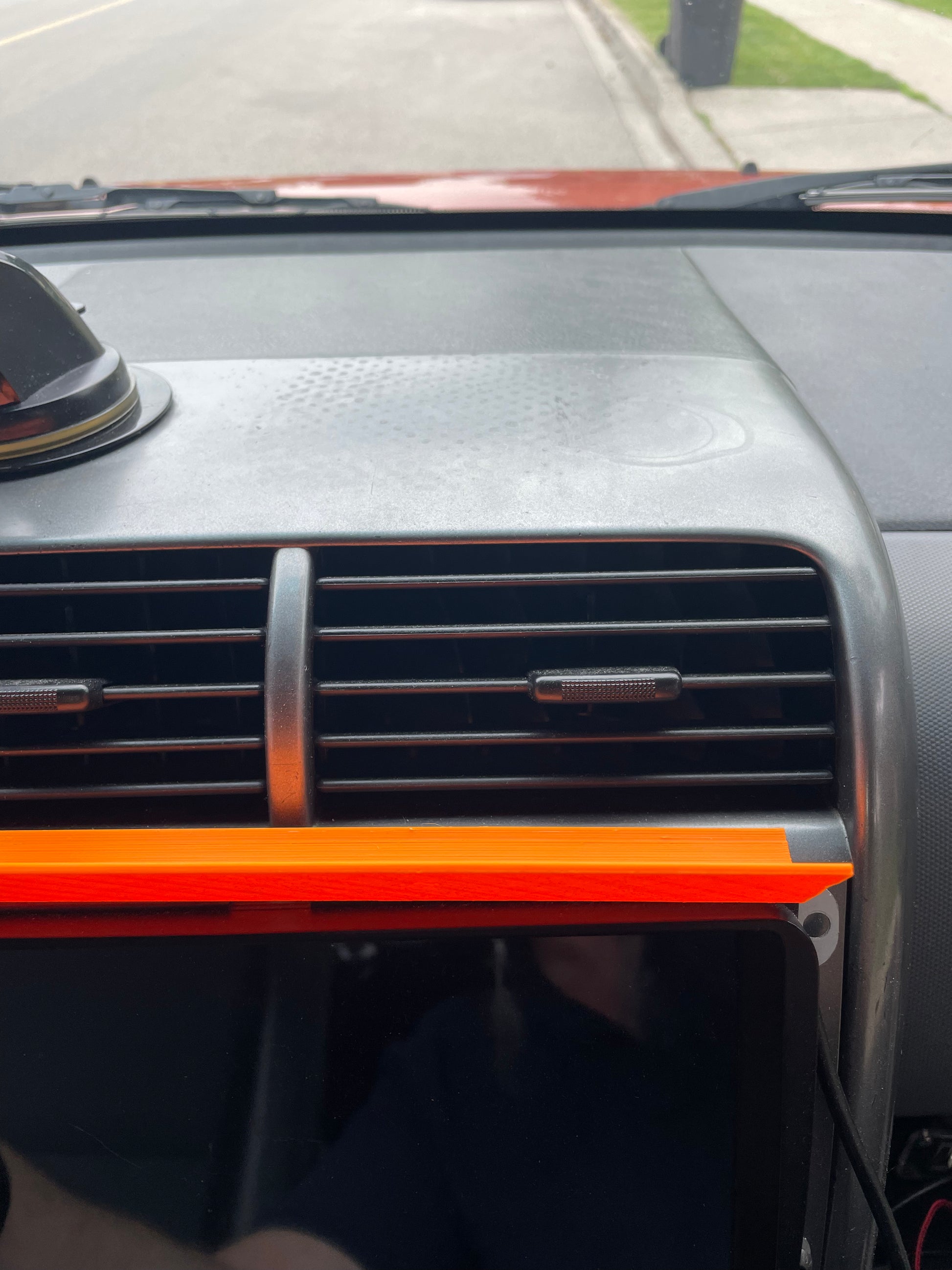 Car dashboard with AC vent, orange trim, and display screen.