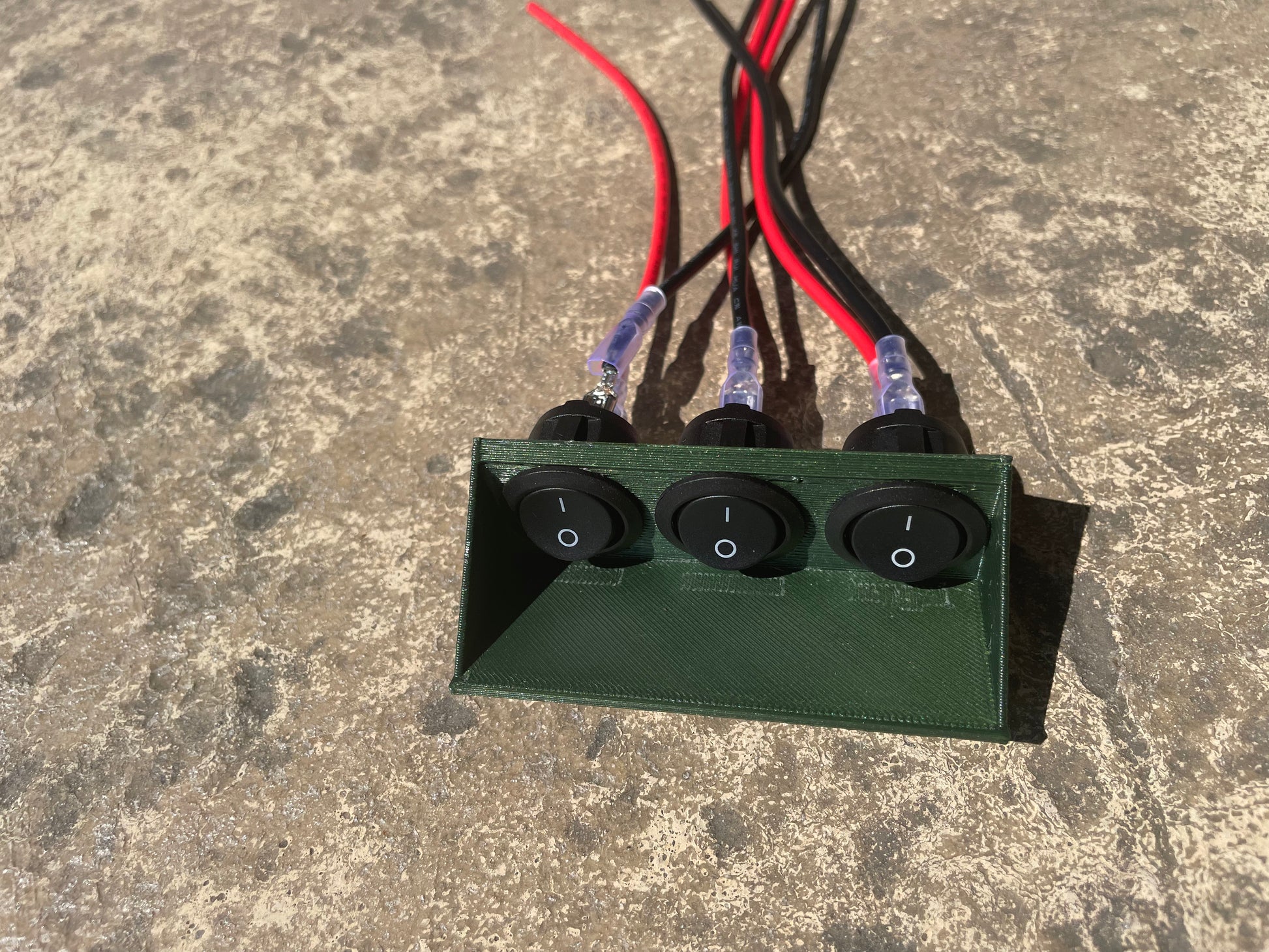 Green switch box with three toggle switches and attached wiring.