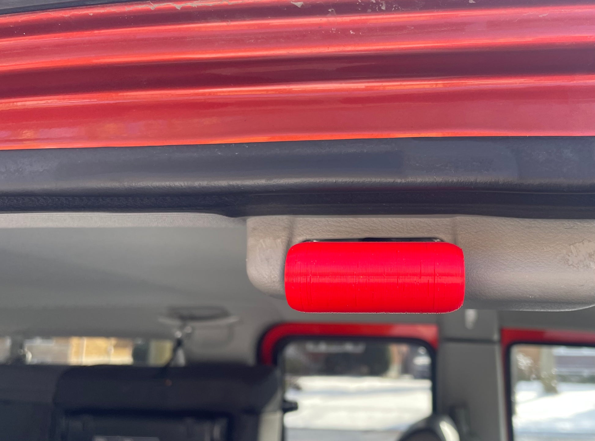 Red 3D printed grab handle on a car's interior.